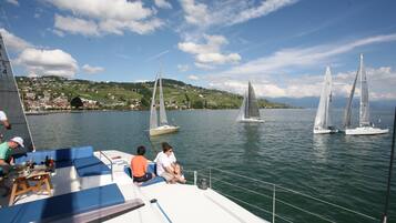 A boat with a blue and white deck, people sitting and standing, and sailboats in the background.