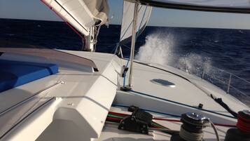 A sailboat's deck with a white hull, blue cushions, and a view of the ocean.