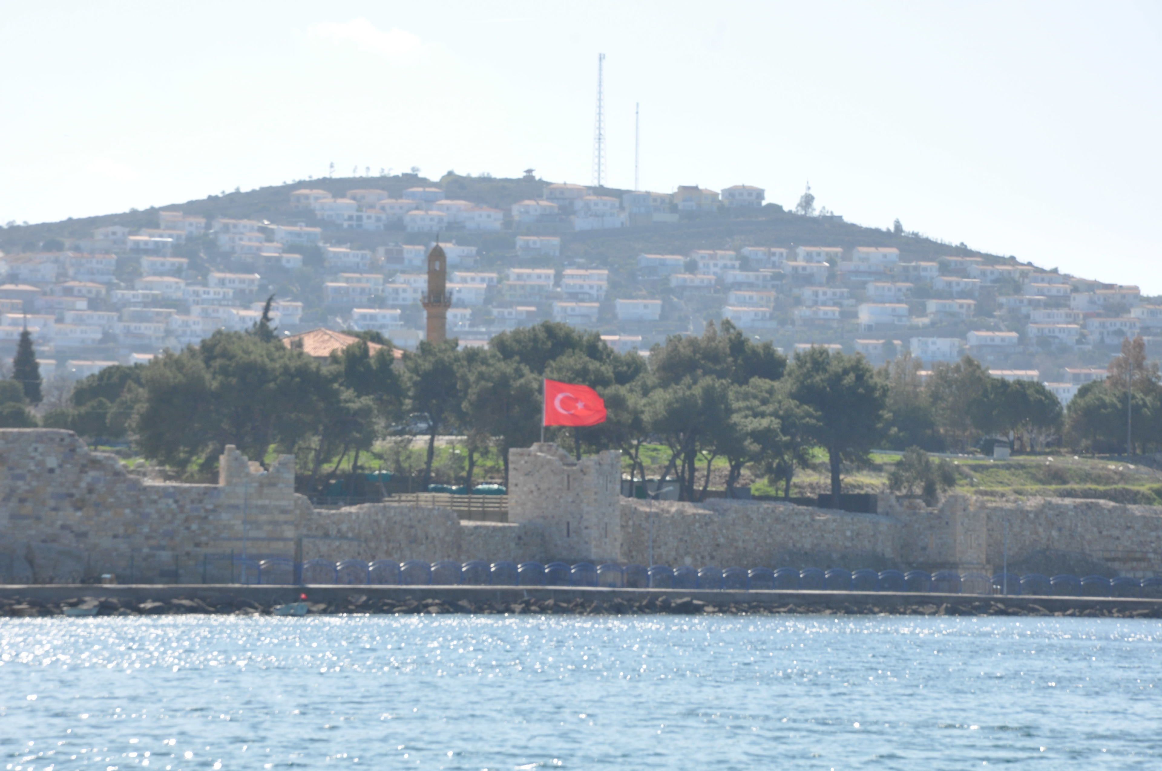 A coastal cityscape with a prominent hill, a flag, and a stone wall.