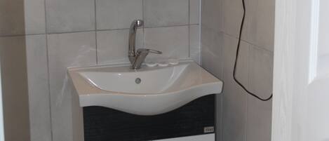 Un baño con un lavamanos blanco, un espejo encima y un tozaleta en la pared.