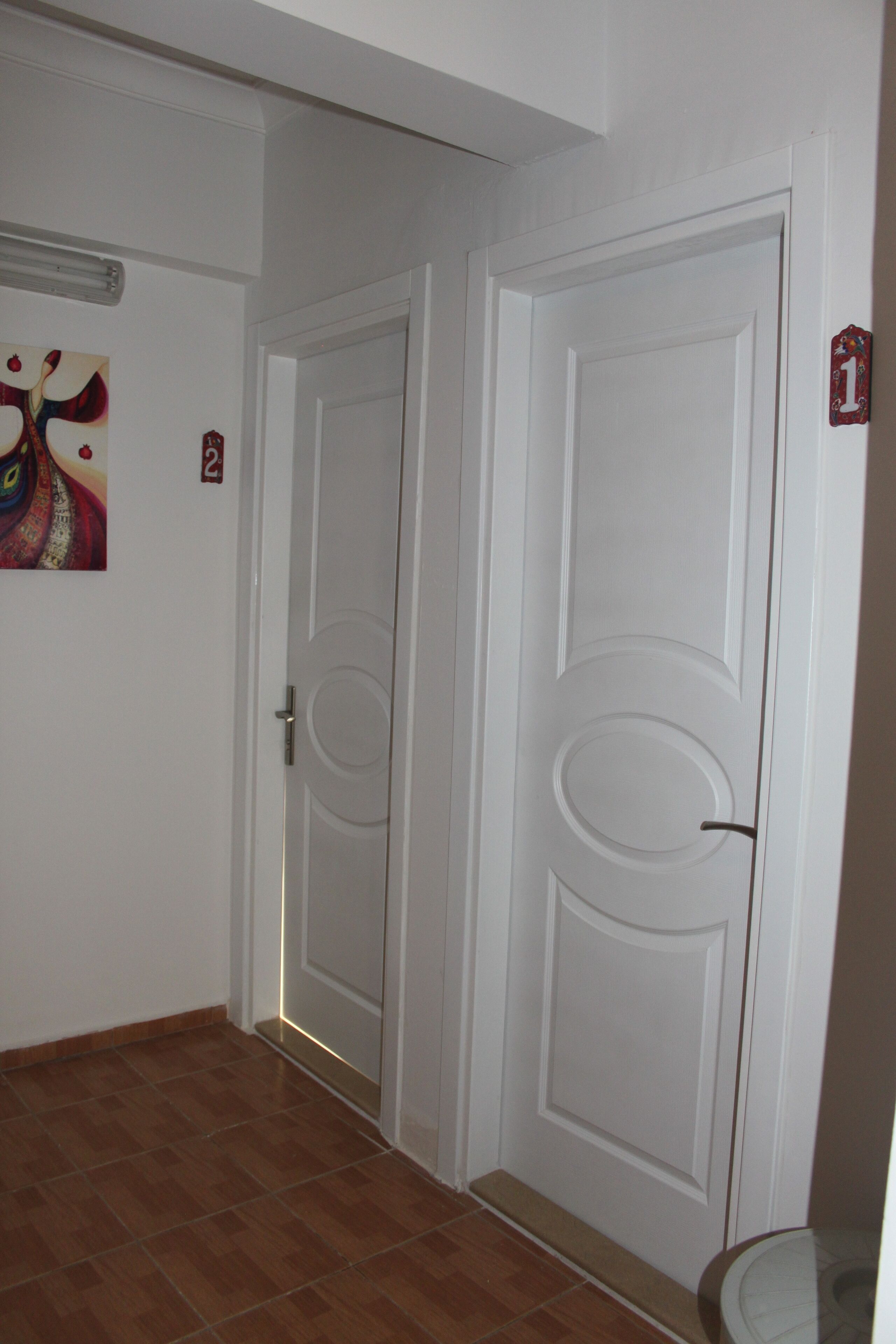 A hallway with two white doors, a number '1' sign, and a colorful painting on the wall.