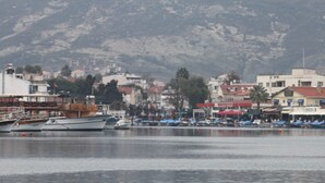 A marina with boats docked, a mountainous backdrop, and buildings with various architectural styles. - Foca Kumsal Hotel (Foça)