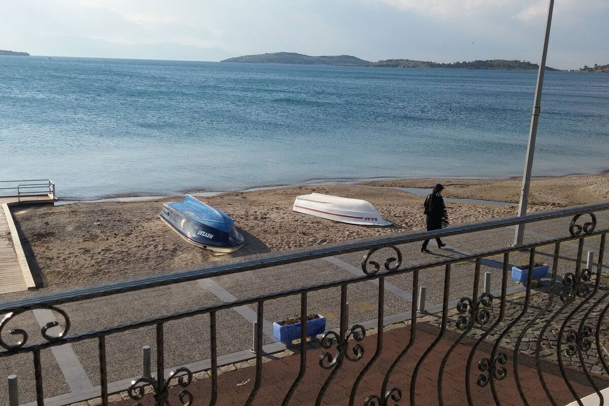 A beach with a wooden pier, a metal railing, and a person walking.