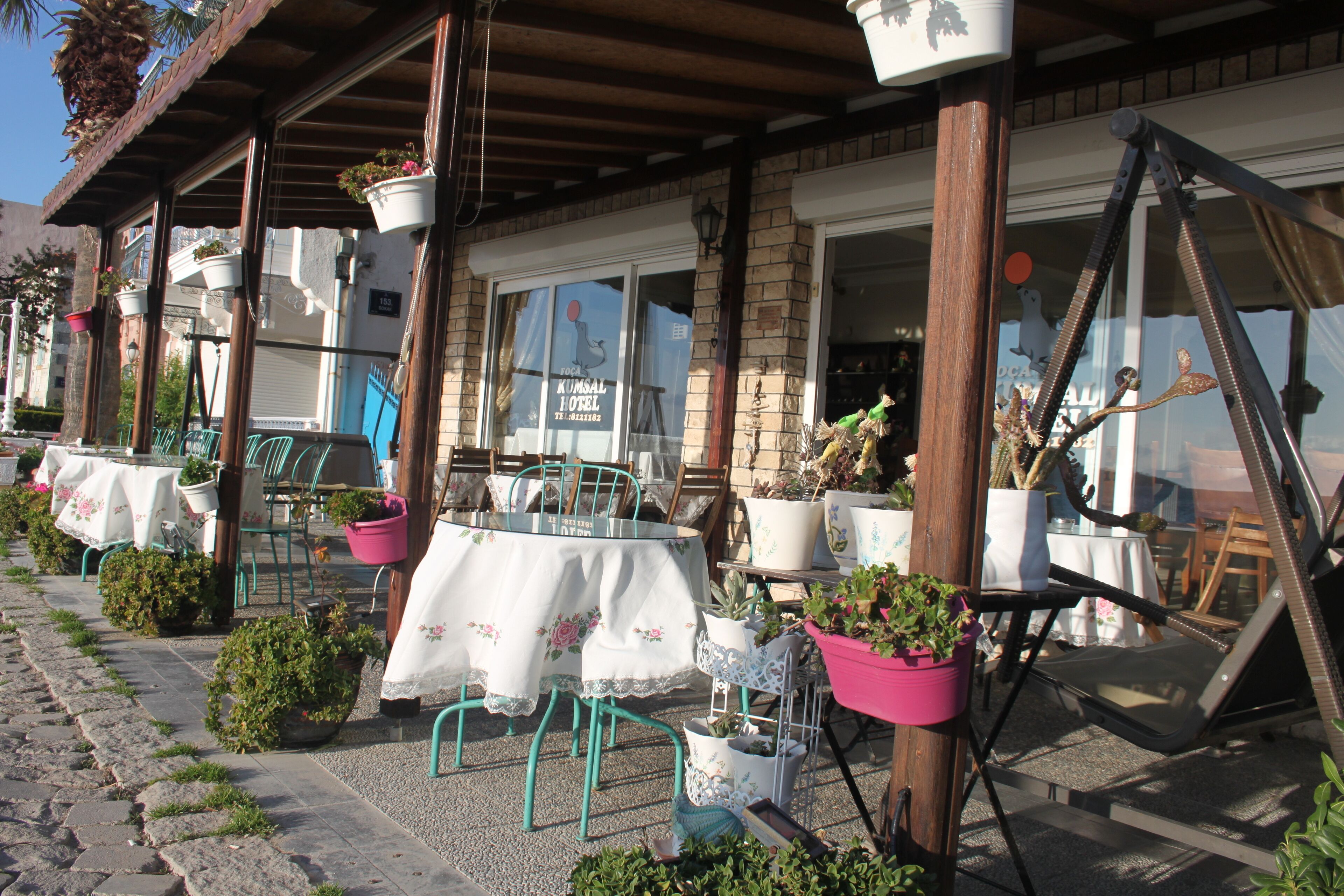 An outdoor seating area with tables and chairs, potted plants, and a brick building facade.