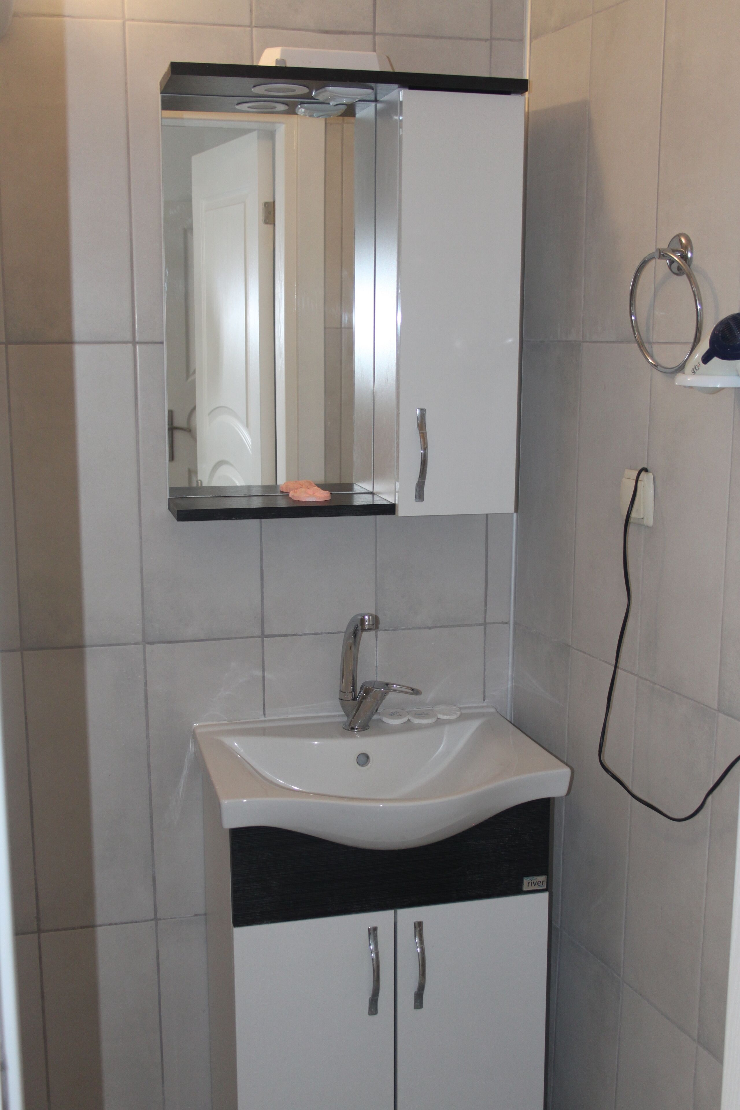 Ein Badezimmer mit einem weißen Waschbecken, einem Spiegel darüber und einem Handtuchhalter an der Wand.
