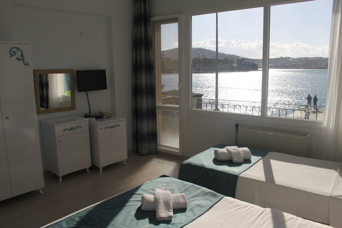 A hotel room with two beds, a TV, a dresser, and a window with a view of the water and mountains.