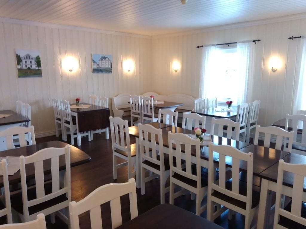 En matplats med vita stolar och bord, väggmonterade lampor och inramade tavlor på väggarna.