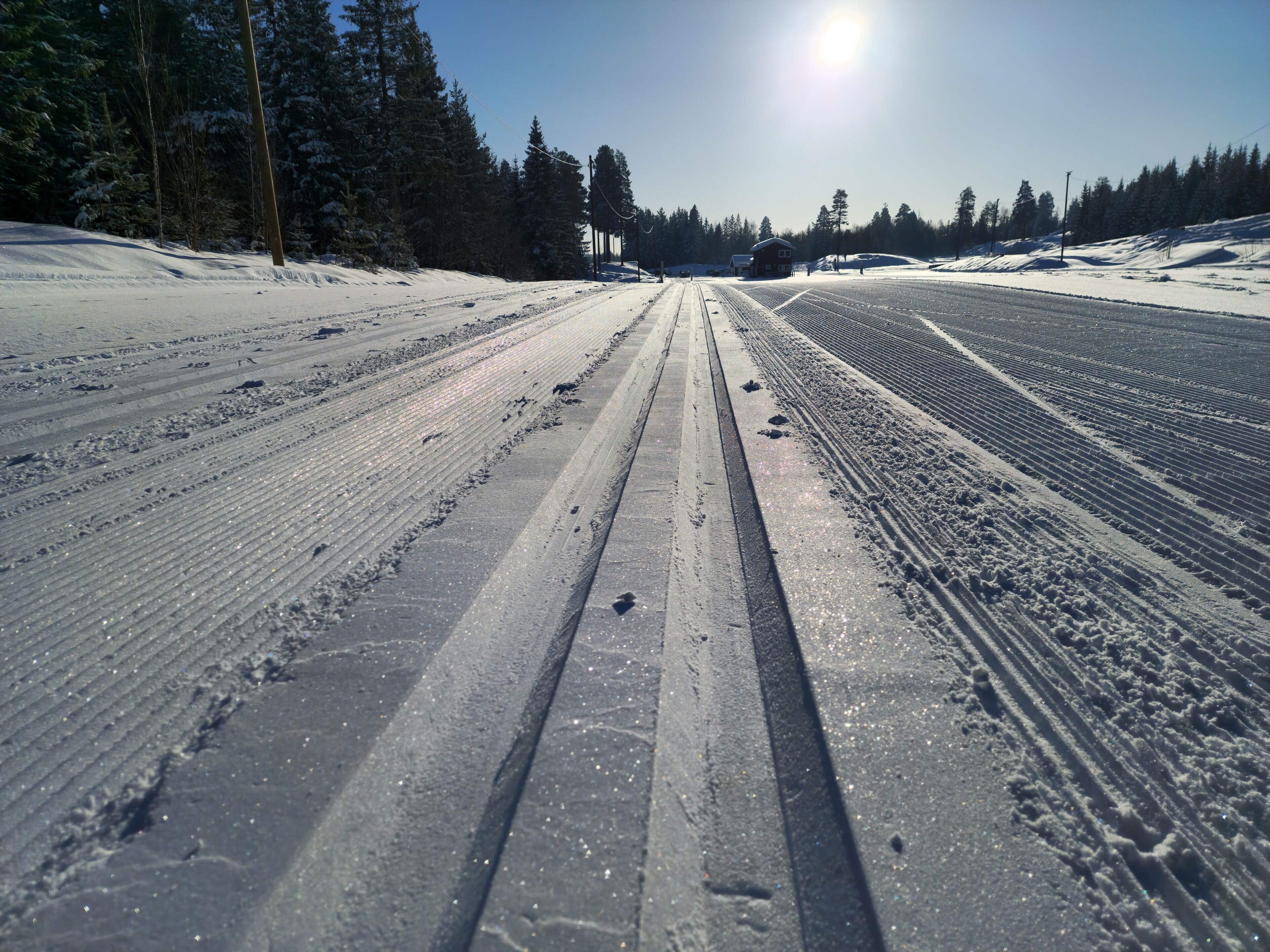A snowy road with tire tracks and a clear sky.