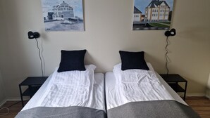 En dubbelsäng med vita sängkläder och mörka kuddar, med två svarta sängbord på var sin sida, varav varje har en lampa.
