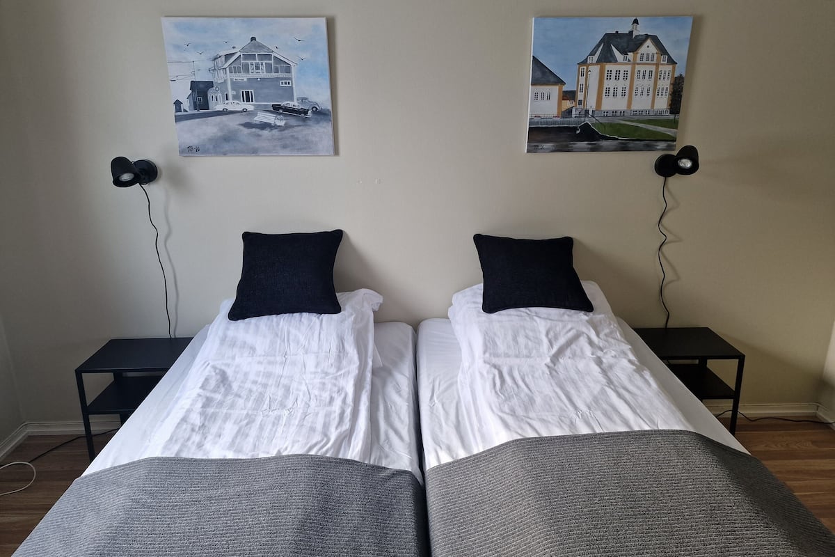A double bed with white linens and dark pillows, flanked by two black nightstands with lamps.
