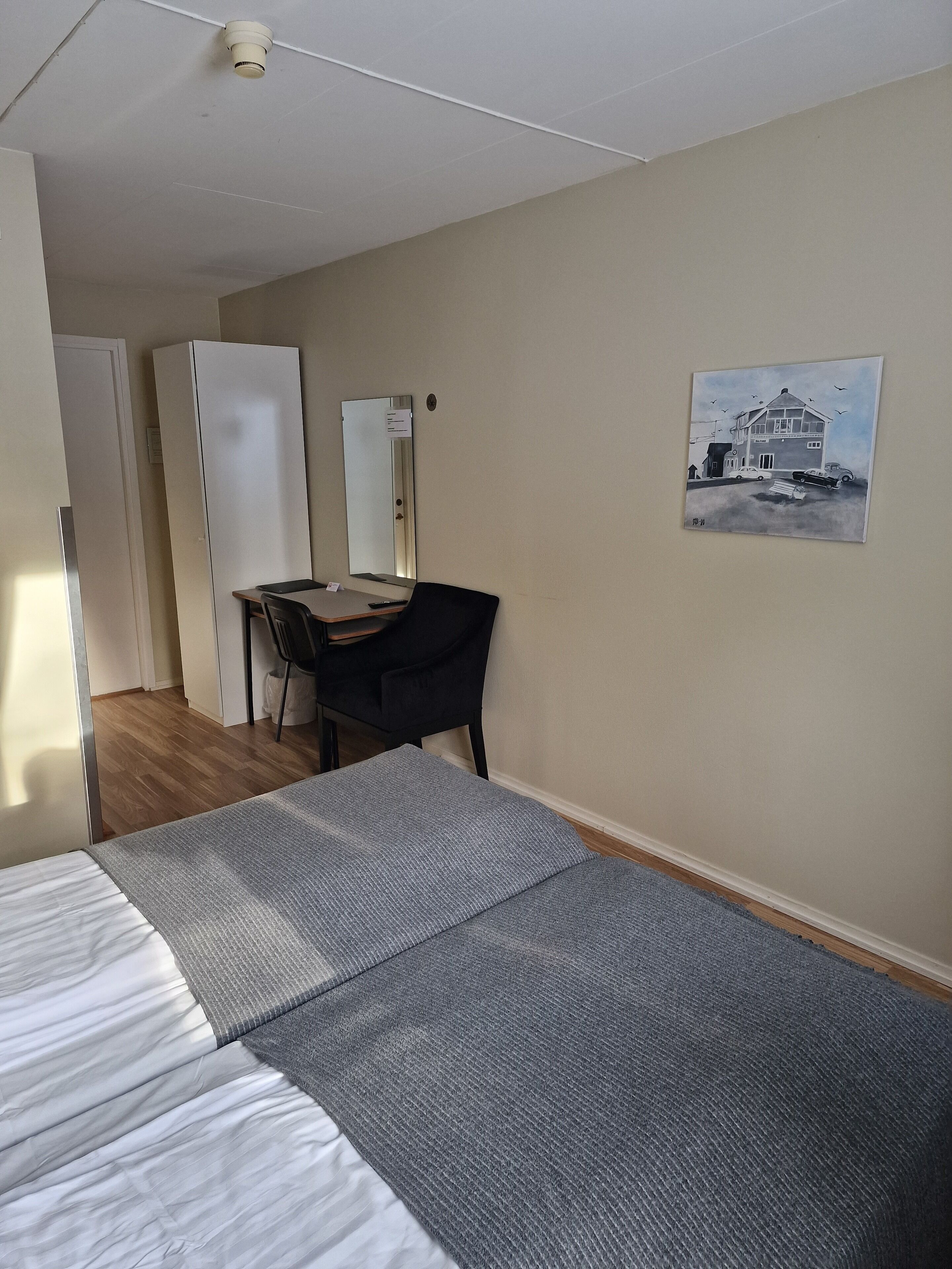 A room with a bed, a desk, a chair, and a painting on the wall.