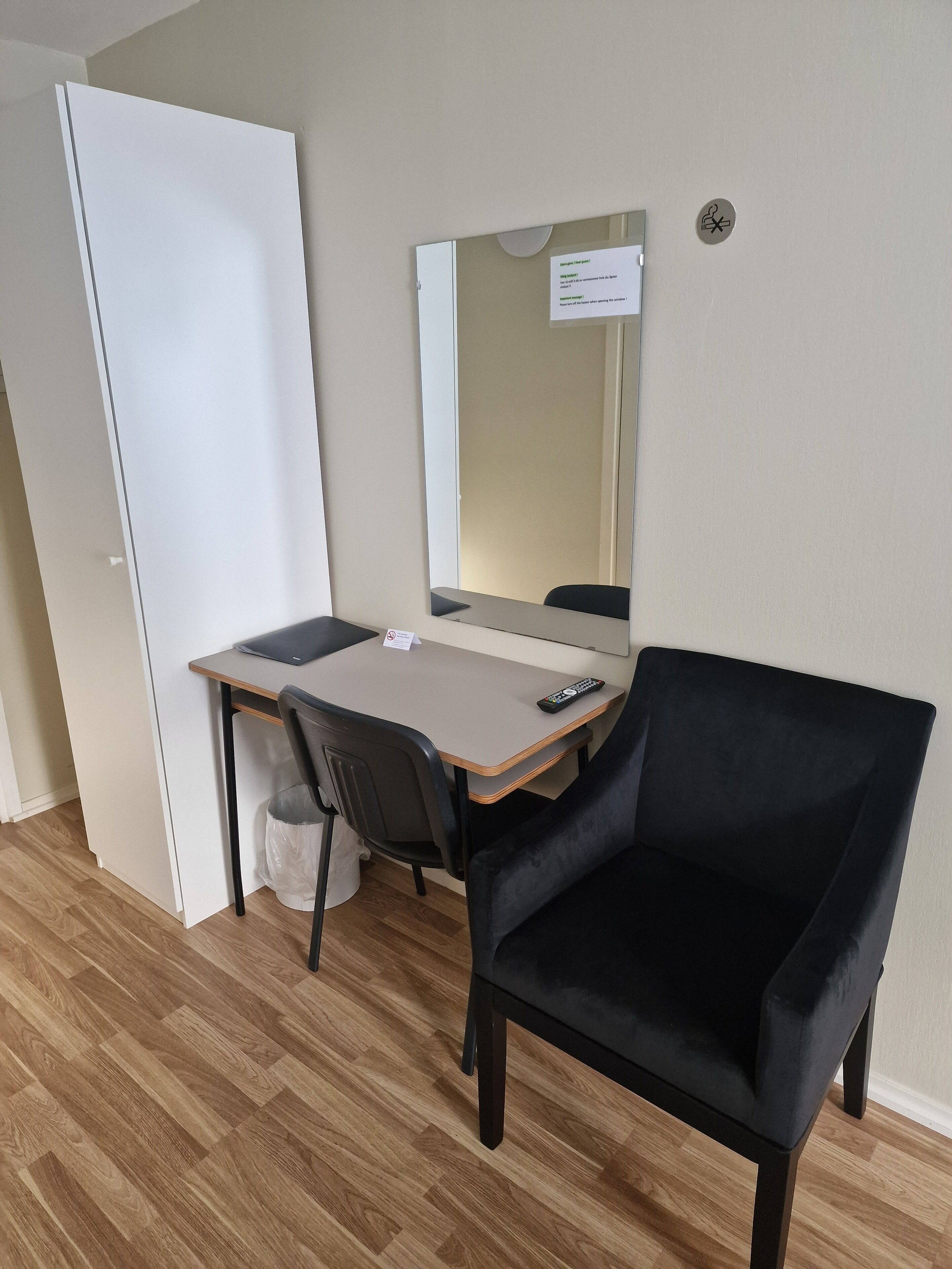 Una habitación pequeña y ordenada con escritorio, silla, espejo y una puerta blanca.