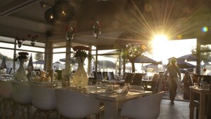 An outdoor dining area with tables set for two, surrounded by chairs, and large umbrellas providing shade. - Vesper Hotel (Noordwijk)