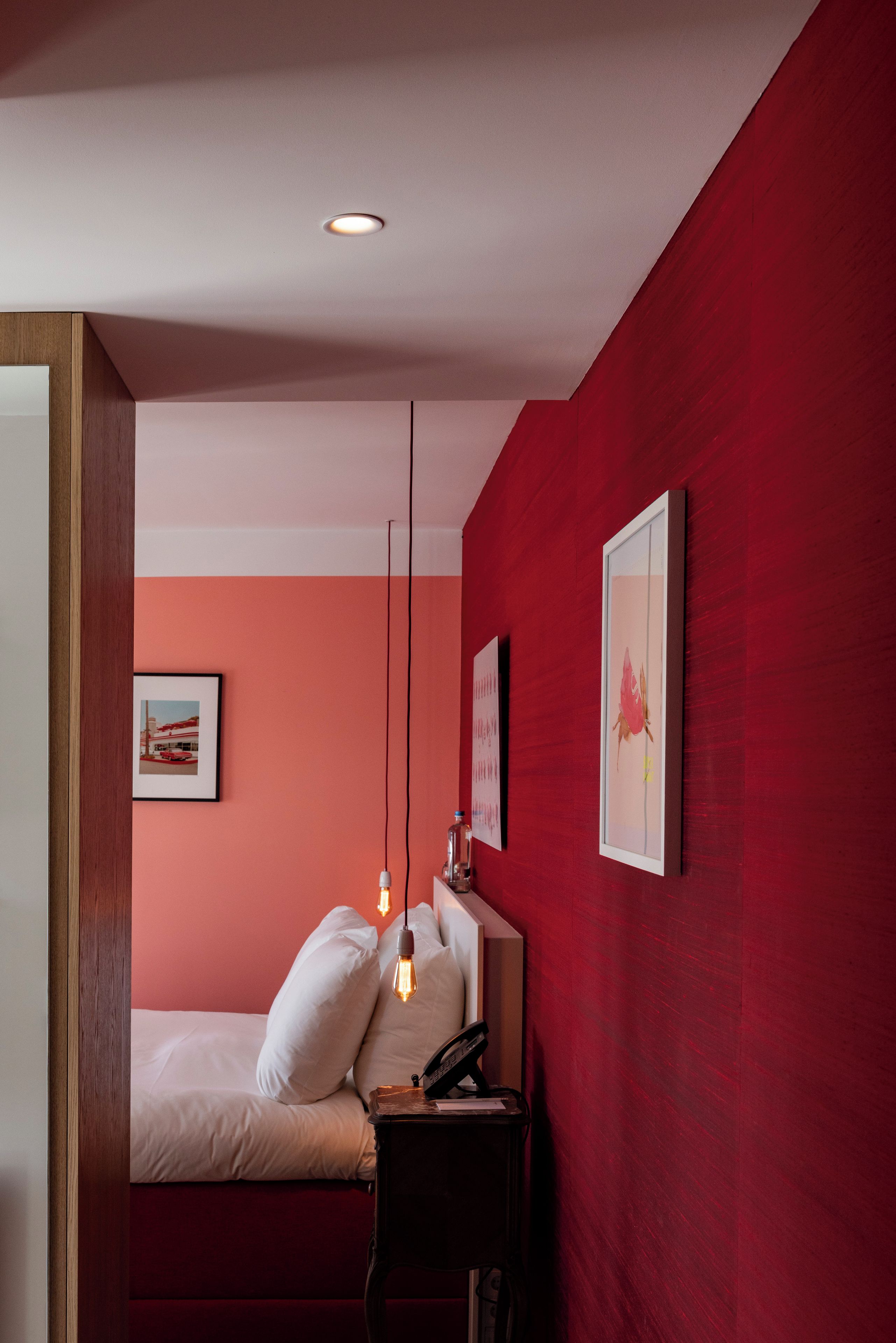 Een slaapkamer met een bed, nachtkastje, lamp en kunstwerk aan de muur.