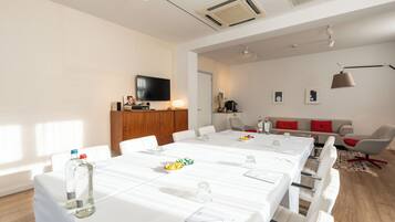 A modern conference room with a long table, white chairs, and a television on the wall.