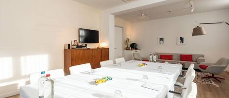 Una sala de conferencias moderna con una mesa larga, sillas blancas y una televisión en la pared.