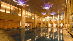 A spacious indoor swimming pool with clear water, surrounded by stone walls and large windows.