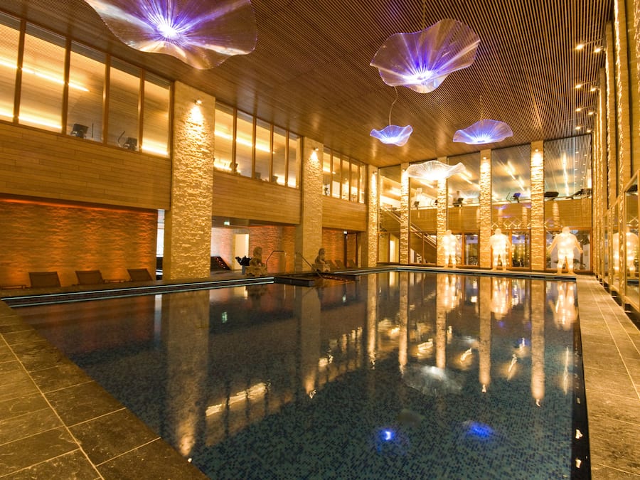 Une vaste piscine intérieure à l’eau claire, entourée de murs en pierre et dotée de grandes fenêtres.