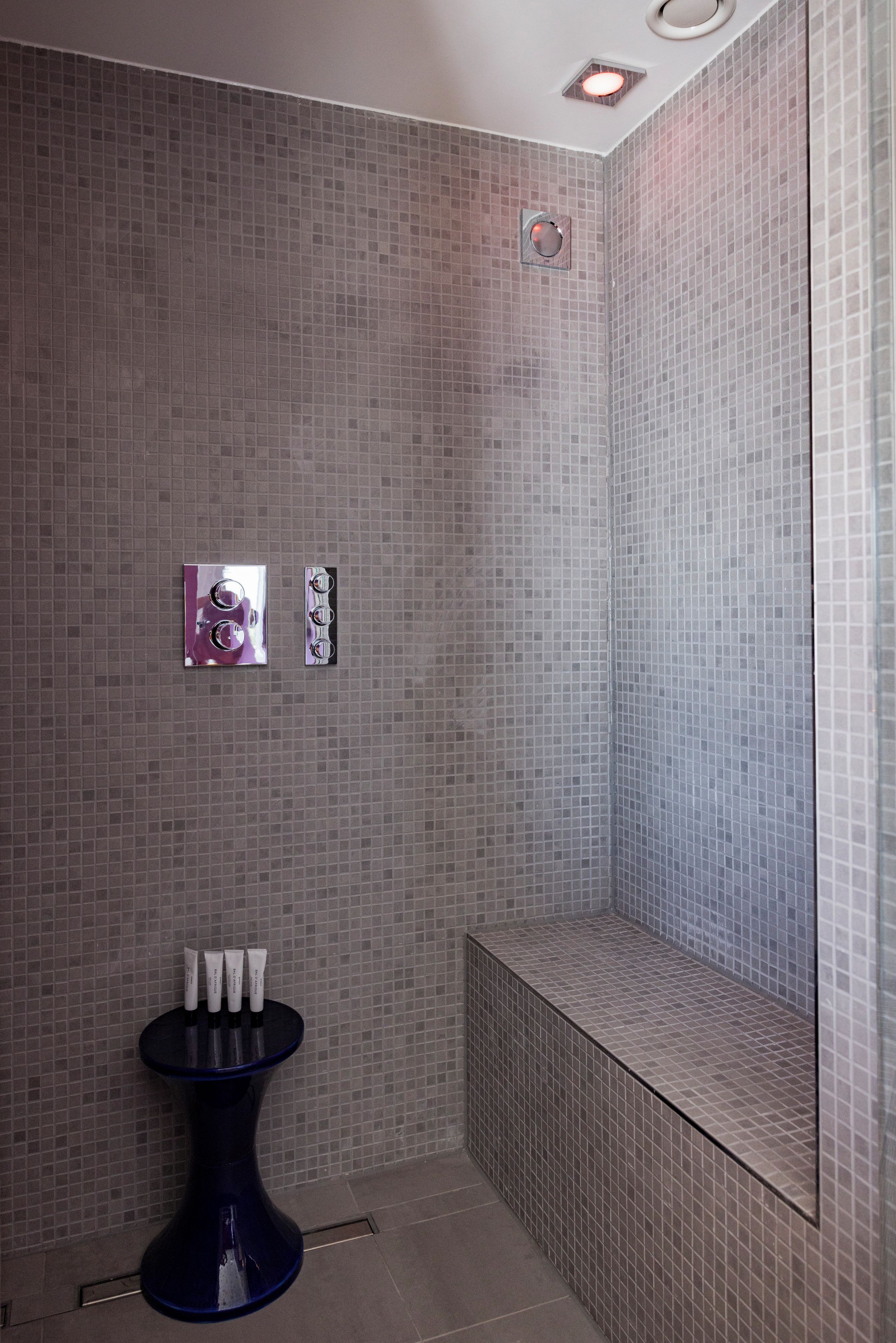 Een badkamer met een betegelde muur, een klein wastafelmeubel met een blauwe wasbak en een spiegel.