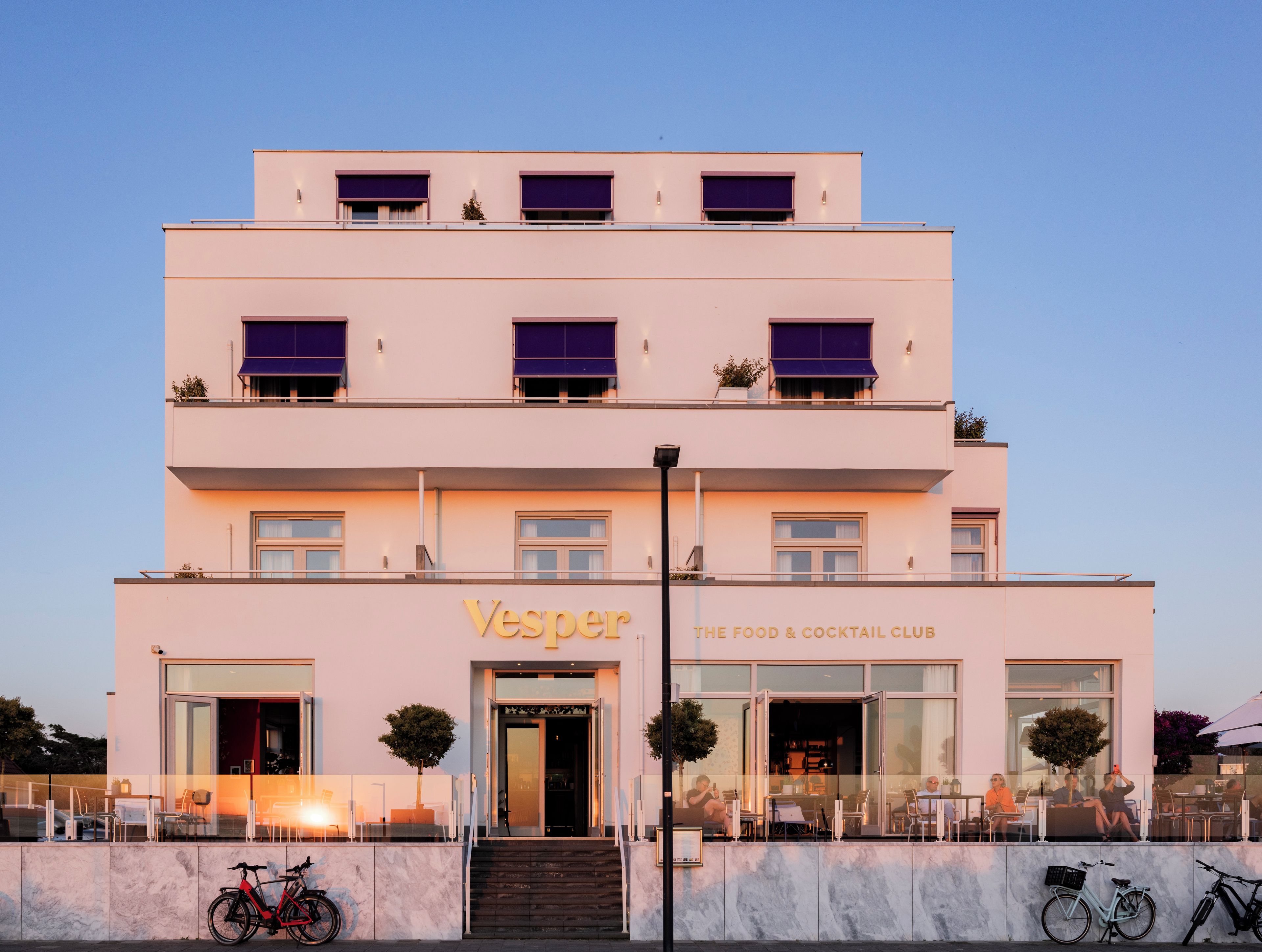 A multi-story building with a sign reading 'Vesper The Food & Cocktail Club.'