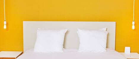 A bed with white bedding and pillows, a white headboard, and two bedside tables with light fixtures.
