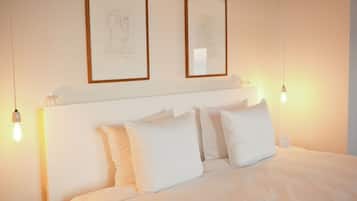 Ein Hotelzimmer mit einem ordentlich bezogenem Bett, zwei gerahmten Kunstwerken an der Wand und zwei Nachttischlampen.