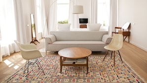 A modern living room with a sofa, two chairs, a round wooden table, a TV, and a painting on the wall.