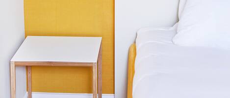 Un dormitorio con una cama blanca, una mesita de noche de madera y una lámpara de pared.
