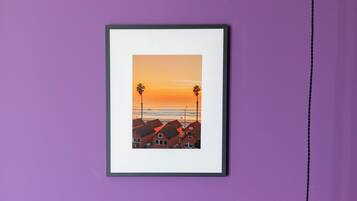 Une photographie encadrée représentant un coucher de soleil sur une plage bordée de palmiers et de maisons, accrochée à un mur violet.