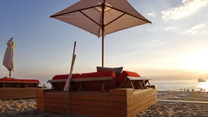 A beach with wooden lounge chairs and a large umbrella. - Vesper Hotel (Noordwijk)