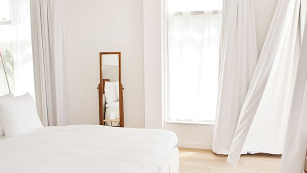 A modern bedroom with a large bed, a nightstand, a mirror, and sheer curtains.