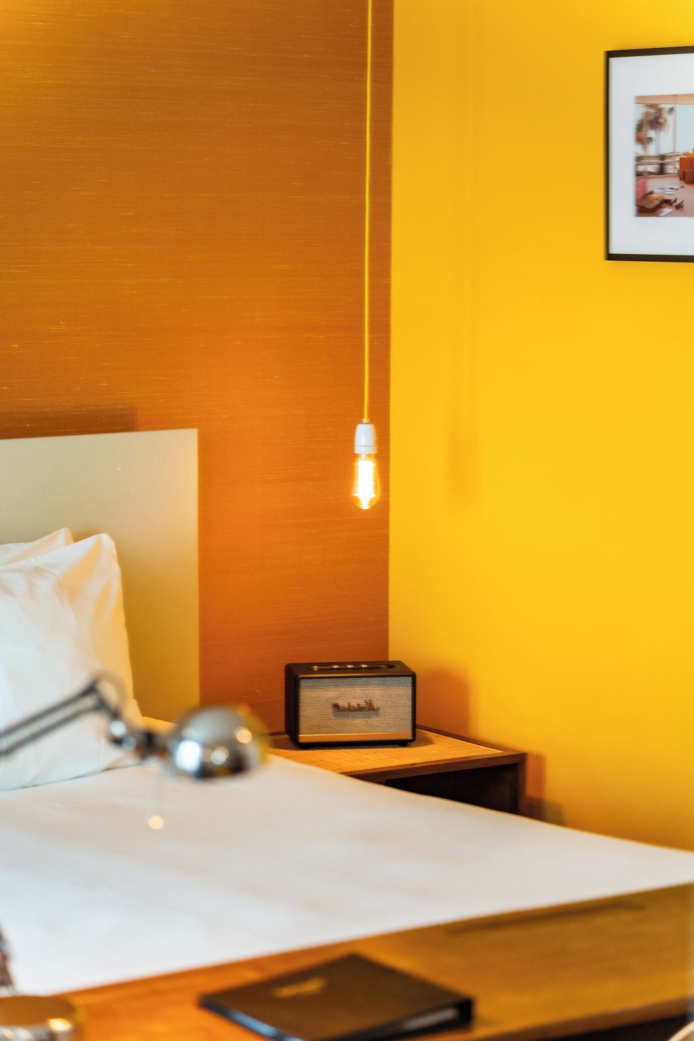A hotel room with a bed, a bedside lamp, a nightstand with a lamp, and a wall-mounted picture.