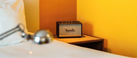 A hotel room with a bed, a bedside lamp, a nightstand with a lamp, and a wall-mounted picture.