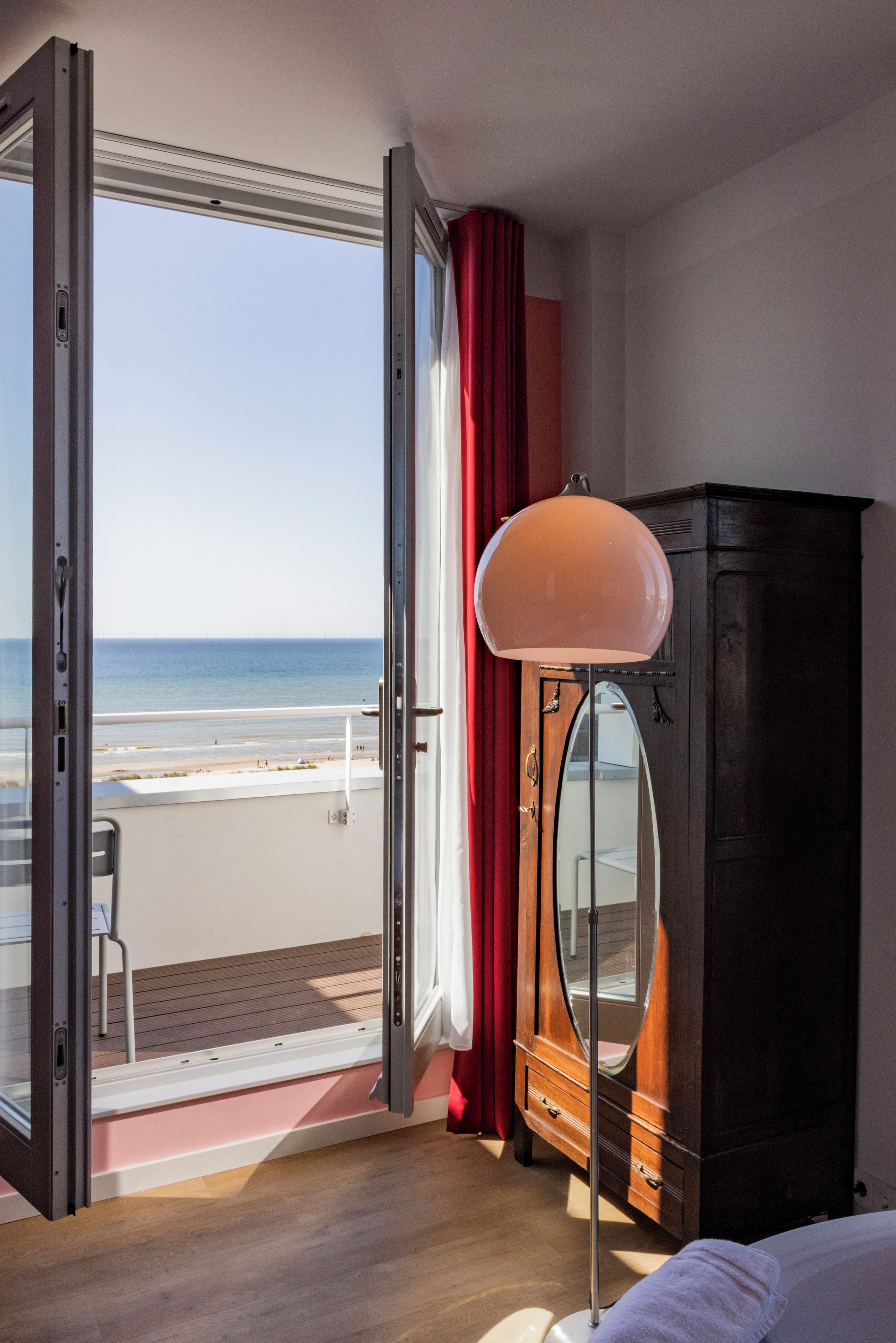 Ein Hotelzimmer mit großem Fenster, einem Holzschrank und Blick auf den Strand.
