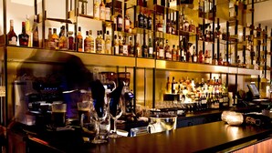A bar area with shelves of various liquor bottles, a coffee machine, and glasses on the counter. - Vesper Hotel (Noordwijk)