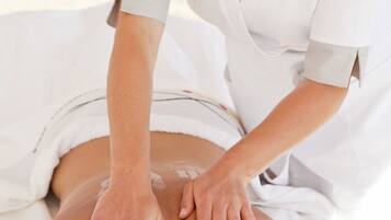 A massage therapy session in a clinical setting with a client lying face down and a therapist applying pressure.