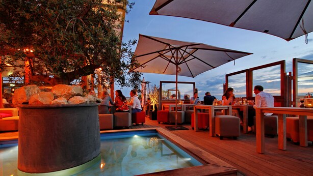 An outdoor dining area with tables and chairs, a pool, and umbrellas. - Vesper Hotel (Noordwijk)