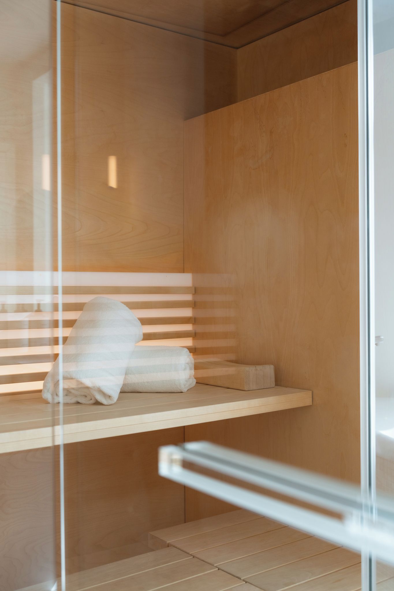 A wooden room with a glass partition, a bench, and a towel on the bench.