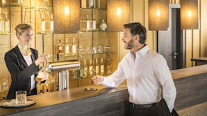 Una zona de bar con un camarero sirviendo una bebida, estantes con botellas y una barra.