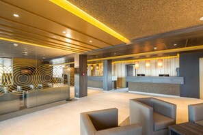 A modern lobby with a reception desk, seating area, and a decorative glass wall. - My Hotel Olching  (Olching)