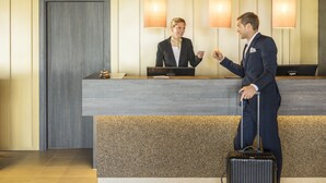 Zona de recepción de hotel con un mostrador de madera, un timbre y una pantalla digital.
