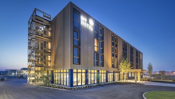 Un moderno edificio de hotel con un llamativo letrero 'MY HOTEL', varios pisos y una zona de entrada bien iluminada.