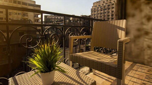 A wicker chair and a potted plant on a balcony with a cityscape view. - The Australian Hostel (Cairo)
