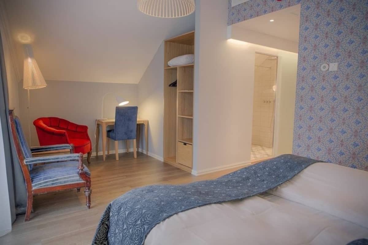 Un dormitorio con una cama, una silla roja, un escritorio pequeño y un armario.