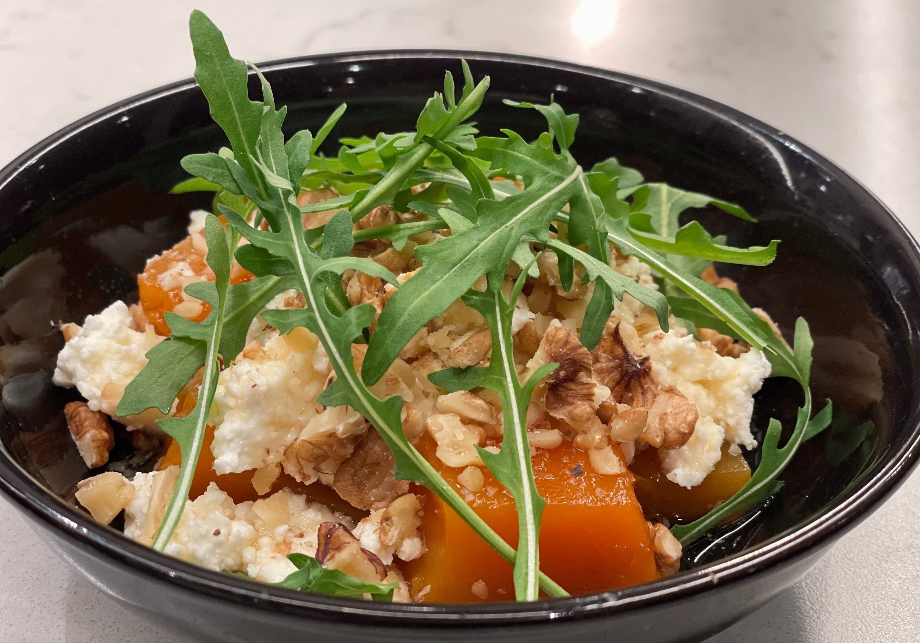 A bowl of food with greens, nuts, and a creamy substance.