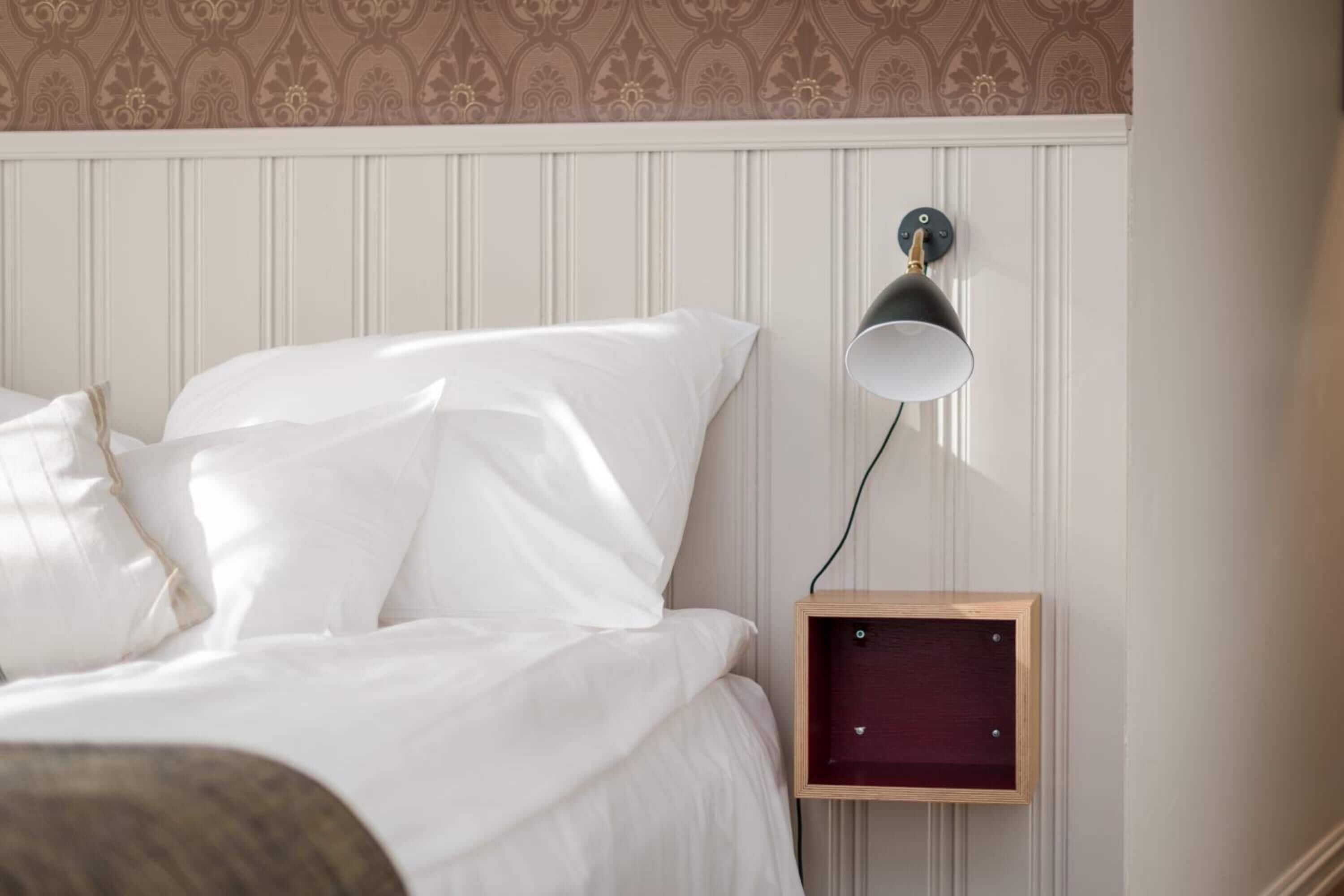 A neatly made bed with white linens and a wooden nightstand with a lamp.