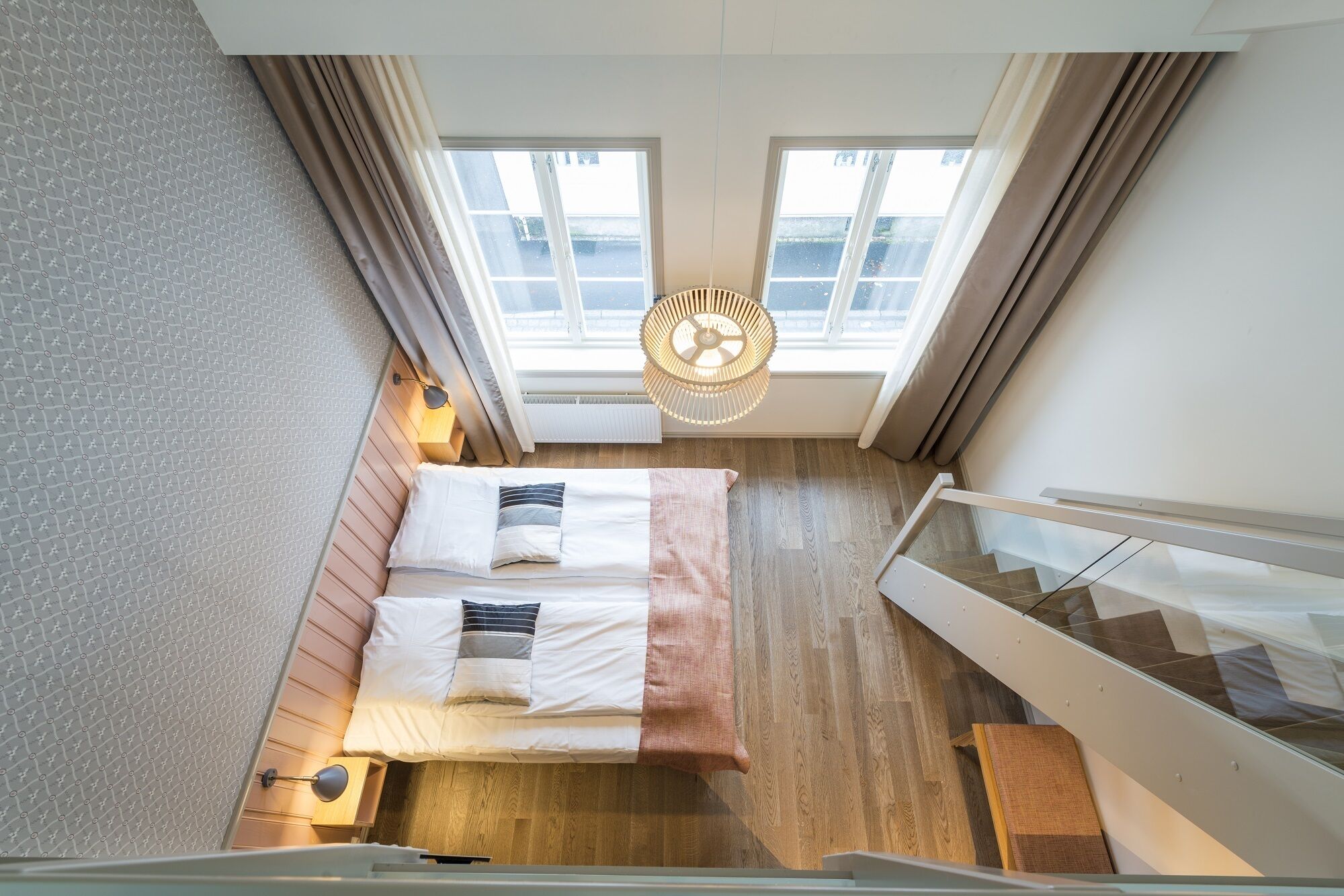 Une chambre à coucher avec un lit, un luminaire suspendu et une vue sur l’extérieur grâce à de grandes fenêtres.