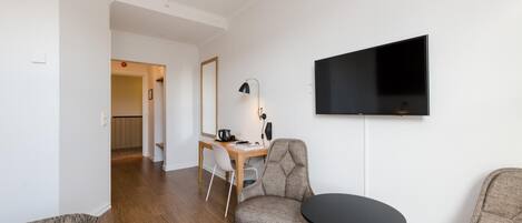A modern living room with a flat-screen TV mounted on the wall, a round coffee table, and two armchairs.