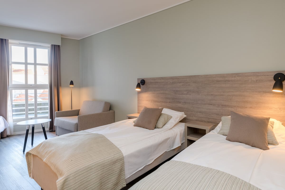 Una habitación de hotel con dos camas, una zona de estar y un ventanal con cortinas.