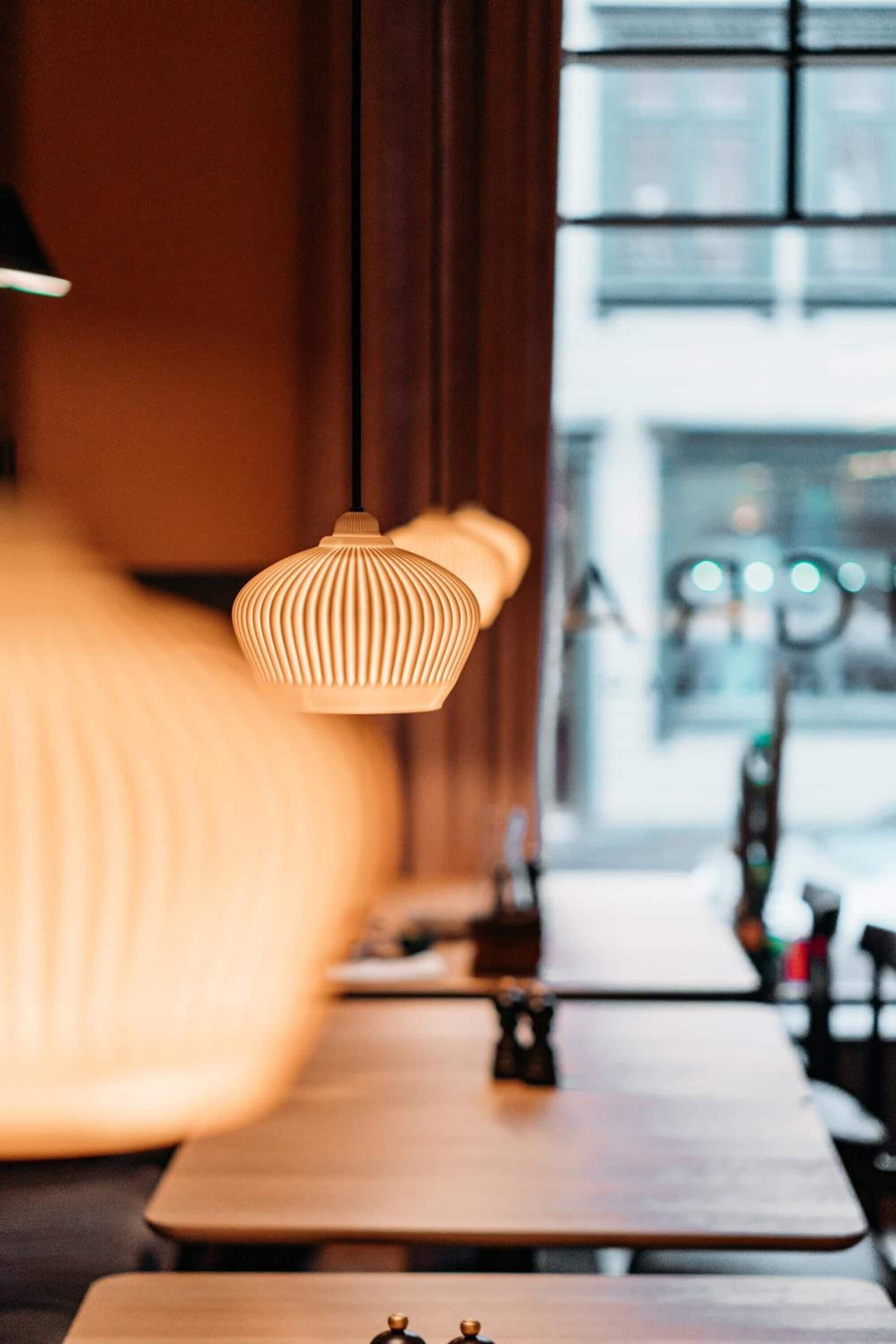 A restaurant interior with wooden tables and hanging pendant lights.